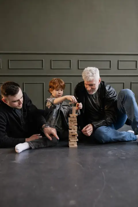 Grandfather, father, and child playing a tabletop block game together