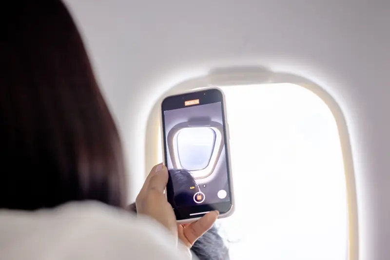 Traveller holding a phone beside an airplane window during a flight