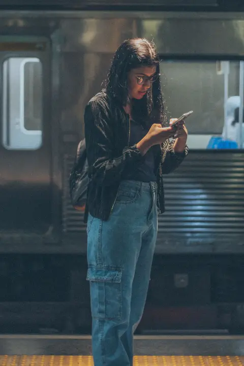 Traveller playing a no WiFi game on an iPhone at a train station