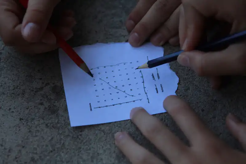 Hands solving a word puzzle together with pencils and paper